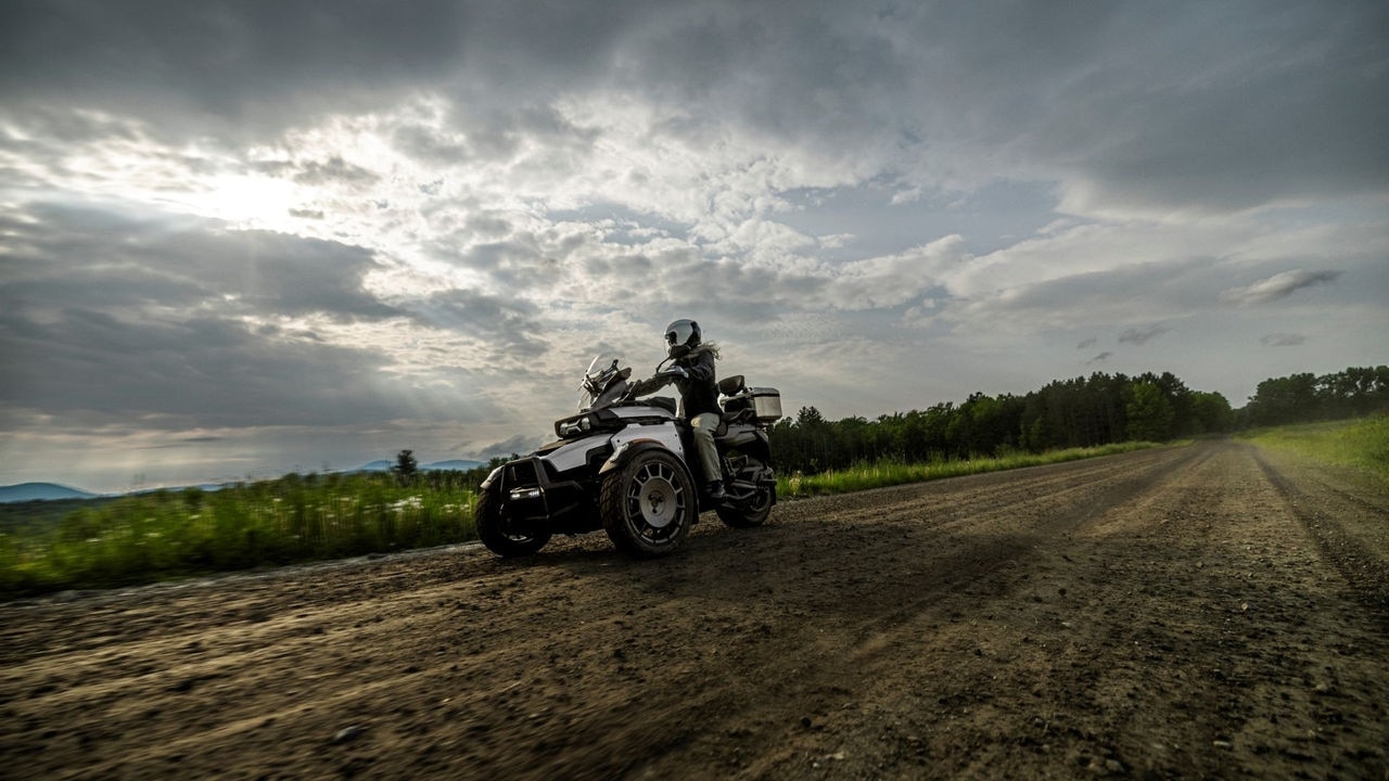 A female rider riding a 2026 Can-Am Canyon 3-wheel motorcycle on a dirt road